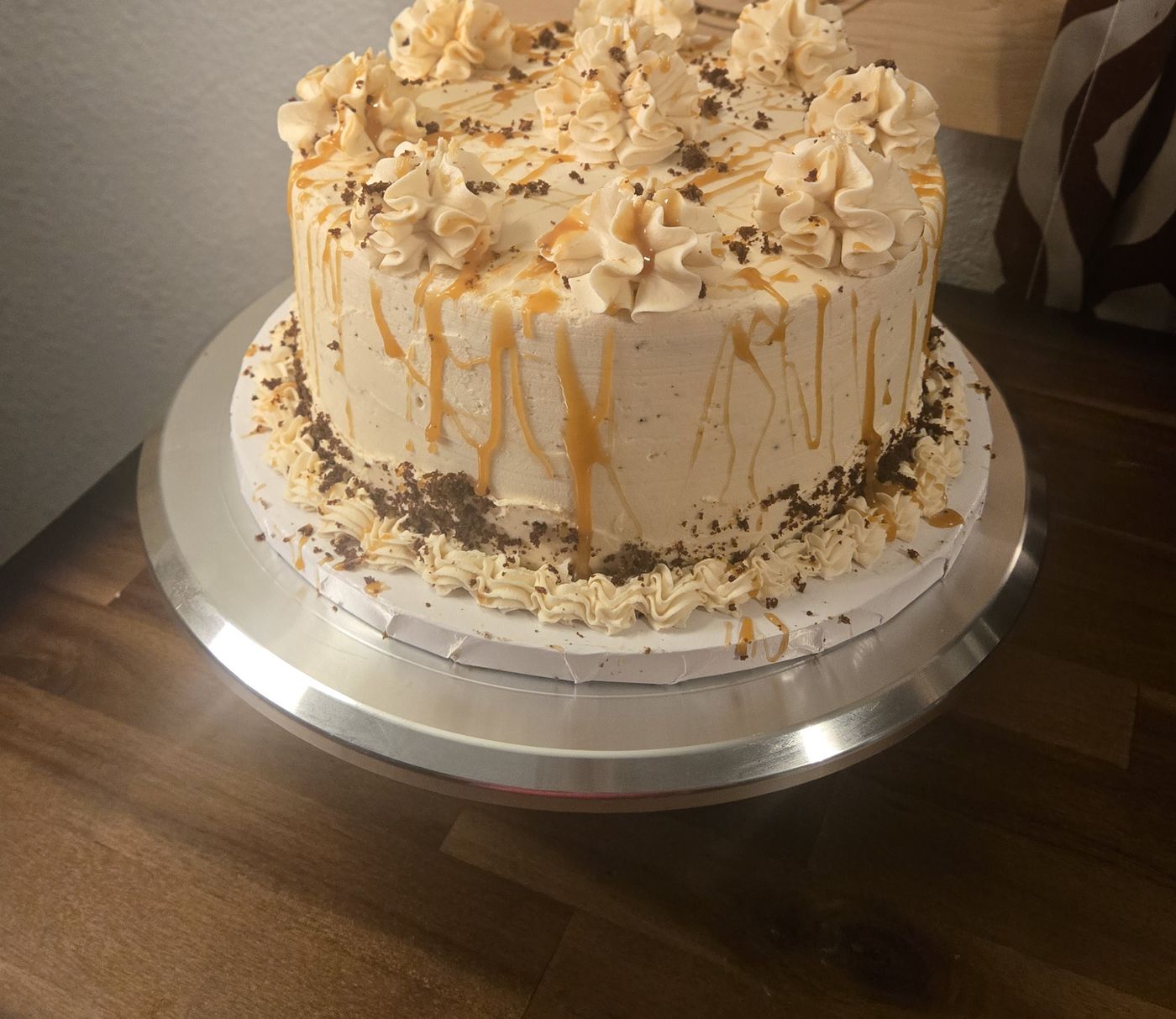 Round layer cake with whipped buttercream rosettes, caramel drizzle and chocolate shavings on a silver cake stand
